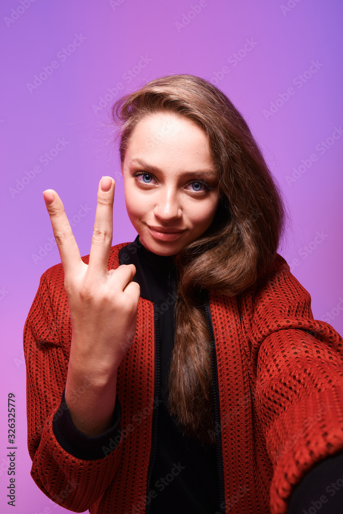 Portrait of happy young girl taking a selfie isolated over trendy neon background. Girl grimaces at camera when taking selfie