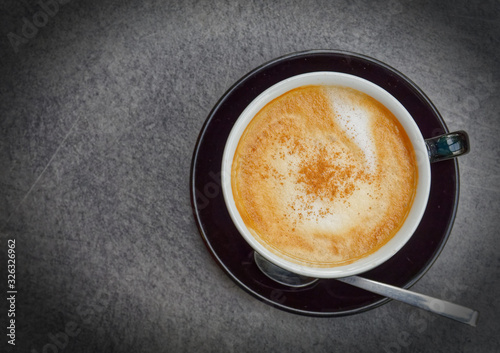 cappuccino coffee cup with spoon top view on grey table, filtered image