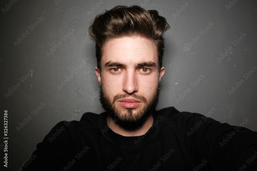 young handsome male with beard, mustache and trendy hairdo, wears casual grey sweater, has serious expression, poses in studio against gray background young handsome male with beard, mustache and trendy hairdo, wears casual grey sweater, has serious expression, poses in studio against gray background