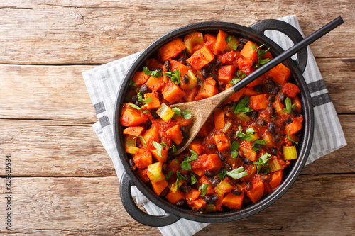 Traditional recipe for chili sweet potatoes and black beans with tomatoes, celery close-up in a pan. Horizontal top view