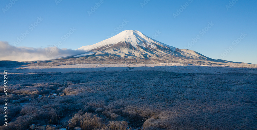 Aerial view of Mount Fuji in winter, iconic snow-capped symbol of Japan at sunrise, snow covered scenery with freezing fog on trees, clear blue sky - landscape panorama of Japan from above, Asia