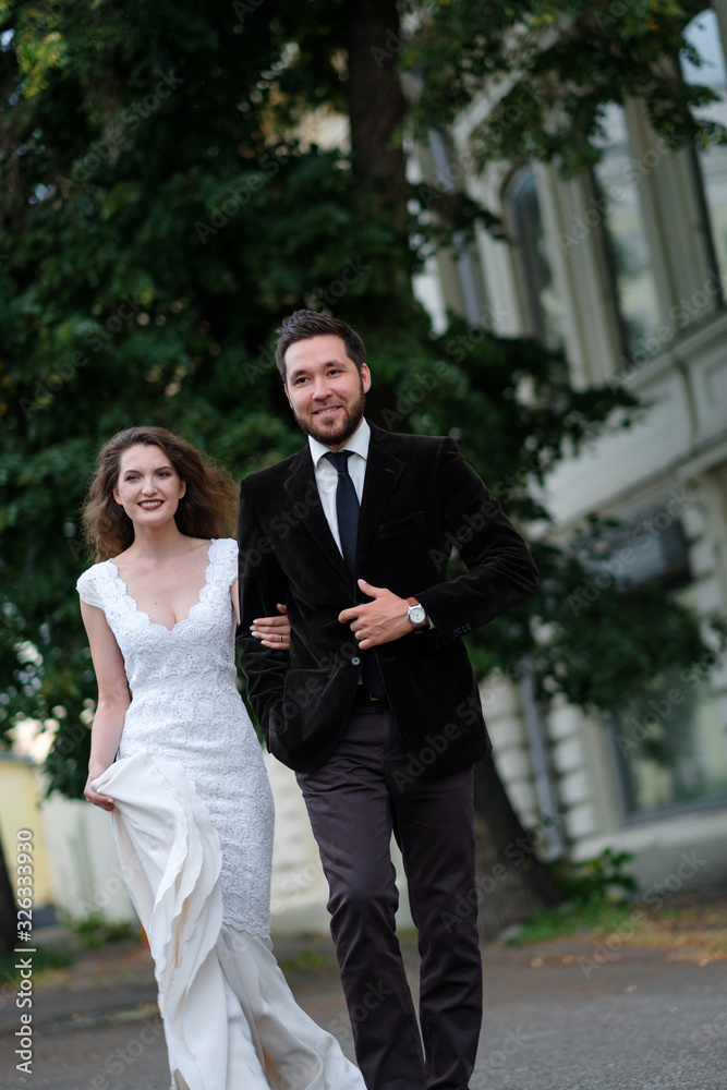 Beautiful wedding couple of newlyweds - red-haired young bride in a white dress and a bearded groom in a black suit. Amazing smiling wedding couple. Pretty bride and stylish groom. Beautiful wedding couple of newlyweds - red-haired young bride in a white dress and a bearded groom in a black suit. Amazing smiling wedding couple. Pretty bride and stylish groom.