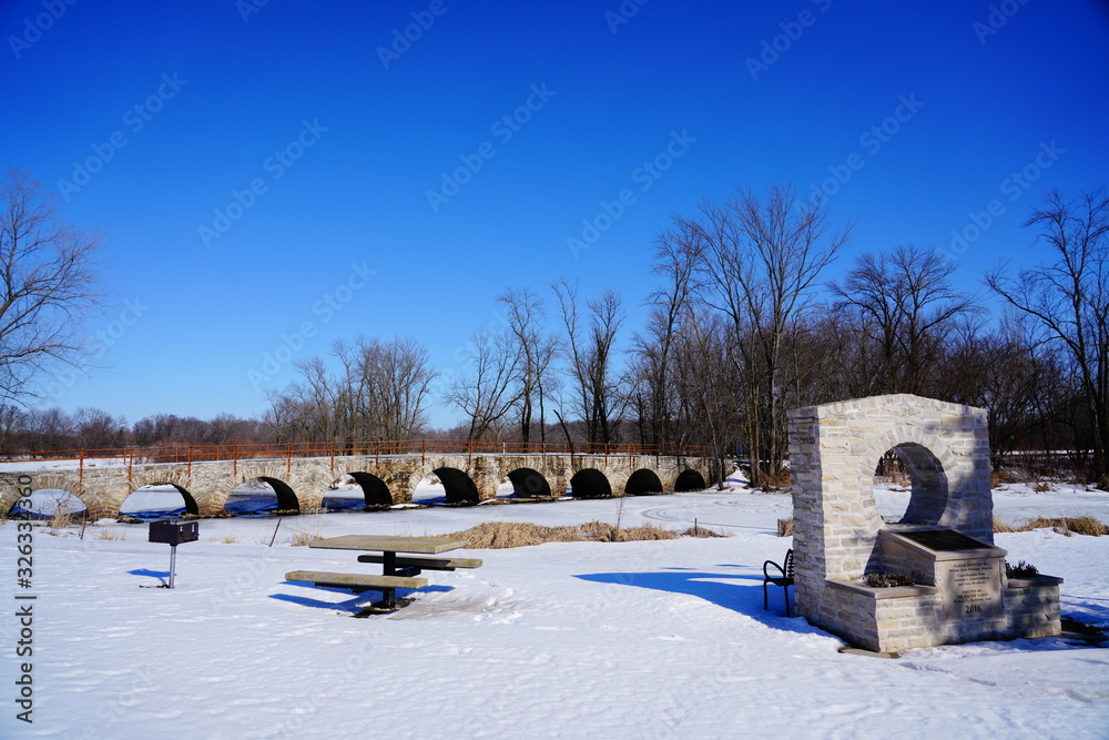 Stone Arch way walking path bridge at Riverside park in St. Cloud, Wisconsin covered in snow during Winter season. 