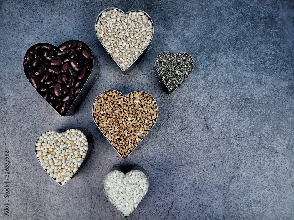 Obraz premium Grain and cereal food selection in heart shaped bowls on dark background. Top view. 