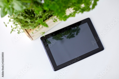 gardening  plants and organic concept - tablet pc computer with herbs and flowers in wooden box on table