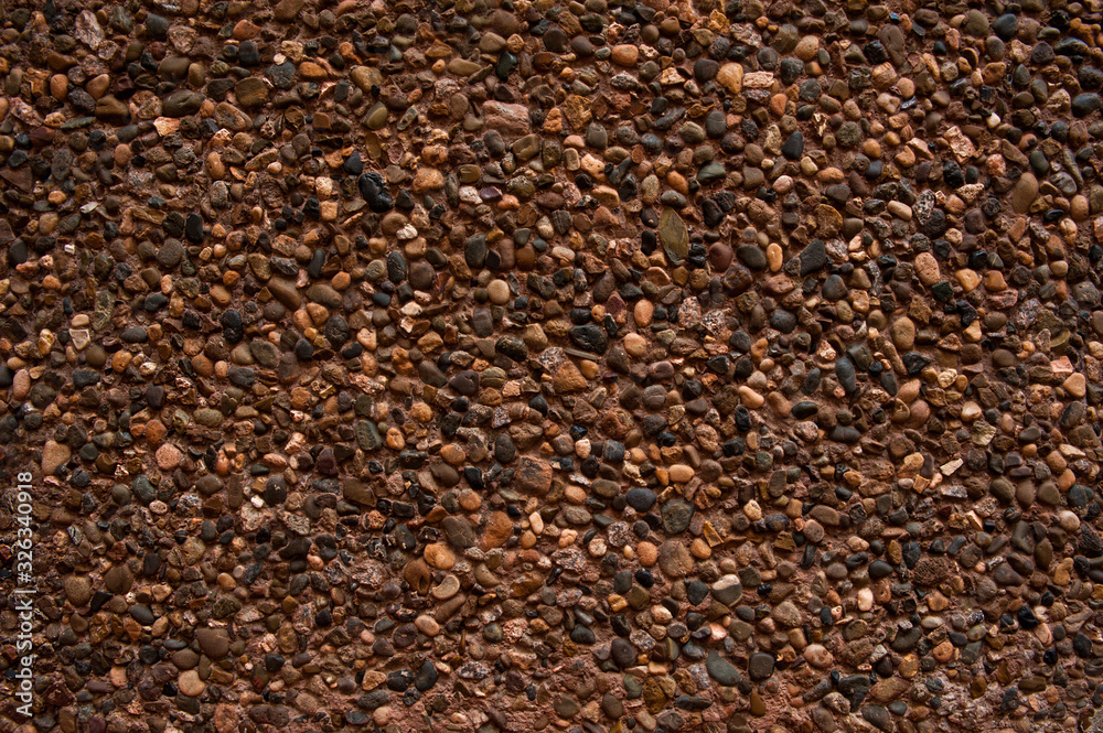 Abstract background. The rough texture, brown concrete wall is decorated with colorful decorative small stones. Texture, structure, background. Abstract background. The rough texture, brown concrete wall is decorated with colorful decorative small stones. Texture, structure, background.