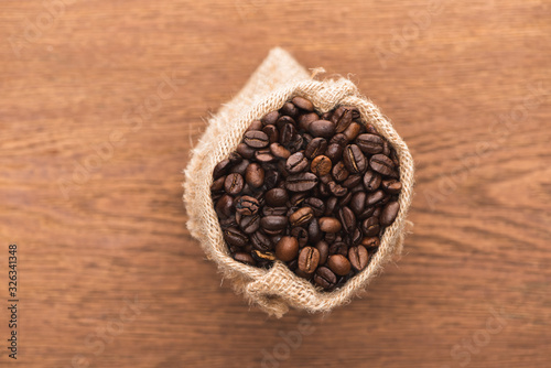 selective focus of fresh roasted coffee beans in sack on wooden surface