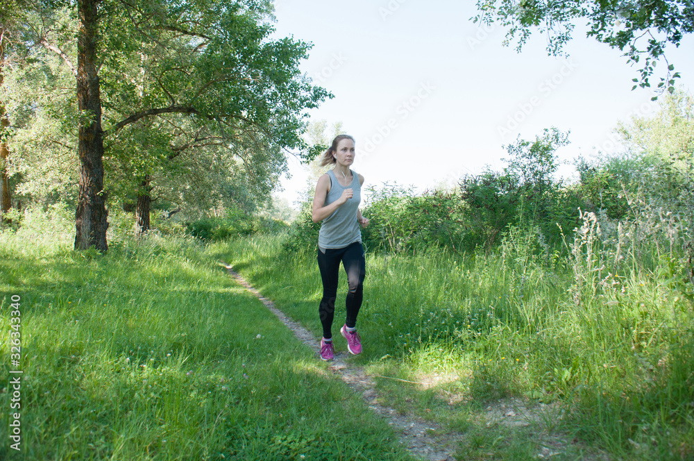 Beautiful, athletic, slender woman with headphones and sports suit runs through the park, summer, sunny morning. Morning jogging and sports Beautiful, athletic, slender woman with headphones and sports suit runs through the park, summer, sunny morning. Morning jogging and sports