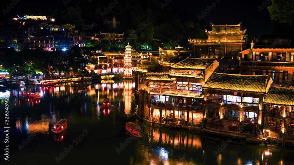 Night scenery view of ancient Chinese town Fenghuang County with illuminated buildings and boats. Hunan, China