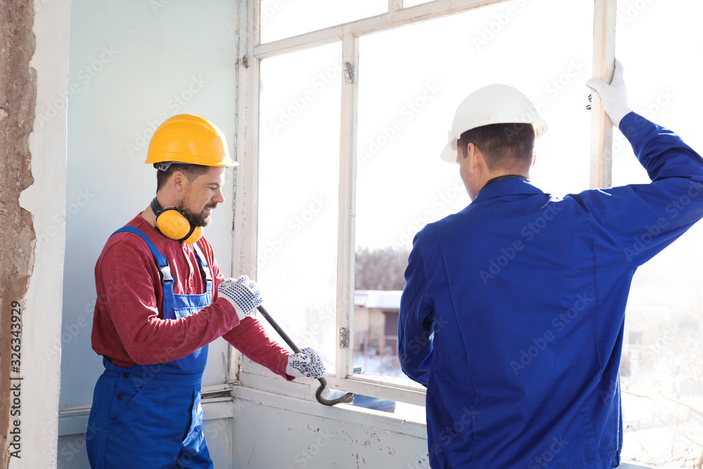 Workers dismantling old window with crowbar indoors