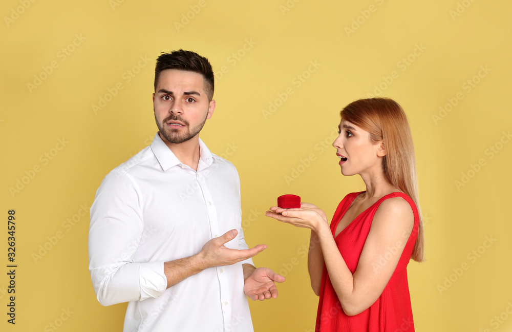 Young woman with engagement ring making proposal of marriage to her boyfriend on yellow background Young woman with engagement ring making proposal of marriage to her boyfriend on yellow background