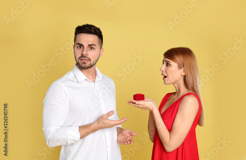 Young woman with engagement ring making proposal of marriage to her boyfriend on yellow background