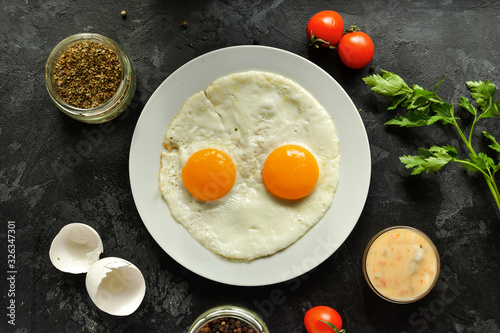 Fried eggs in a white plate. Beautiful fried eggs. Tasty breakfast. Top view, dark concrete background.