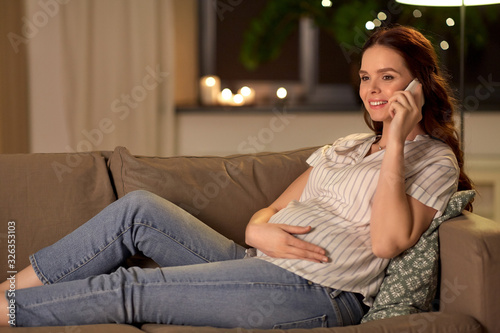 pregnancy, technology and people concept - happy pregnant woman calling on smartphone at home