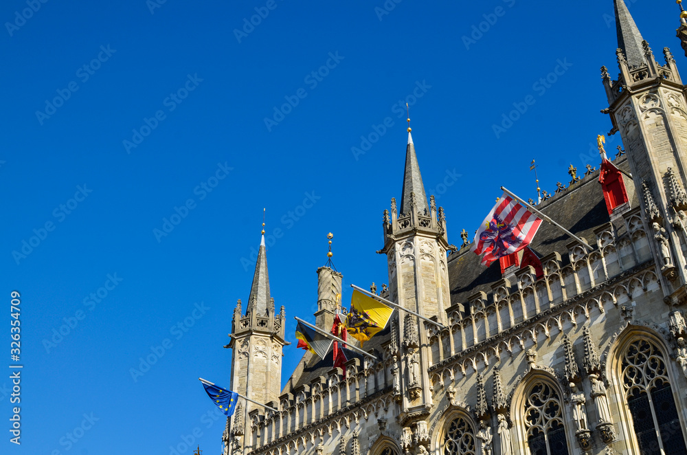 Fototapeta premium Bruges, Flanders, Belgium. August 2019. Burg square is one of the most important. The splendid town hall overlooks it. Detail of the spiers and flags that decorate the facade.