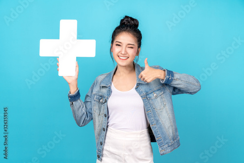 Happiness asian woman smiling, showing plus or add sign and thumb up or like on blue background. Cute asia girl wearing casual jeans shirt and showing join sign for increse and more benefit concept
