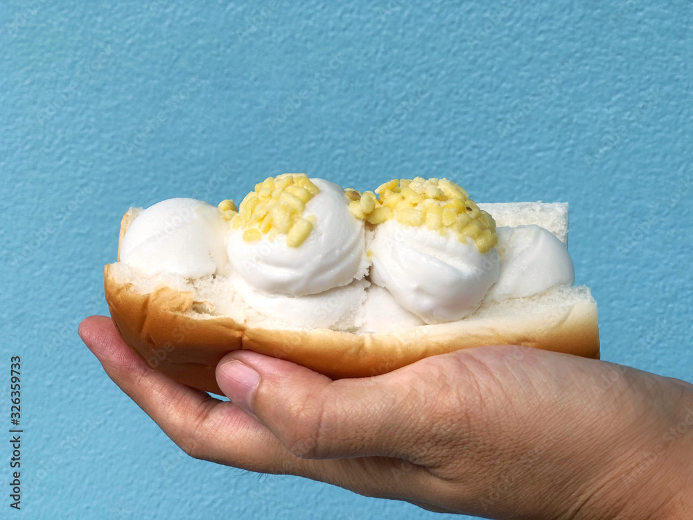 Thai coconut milk ice cream with nut and bread carrying on hand isolated in blue background concrete, Thai street food or Thai dessert concept. Selective focus and blurred background has copy space. Thai coconut milk ice cream with nut and bread carrying on hand isolated in blue background concrete, Thai street food or Thai dessert concept. Selective focus and blurred background has copy space.