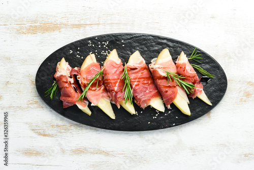 Italian food. Prosciutto with pear and balsamic sauce. Jamon on a black stone plate. Top view.