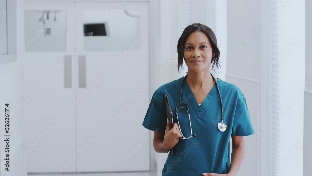 Portrait Of Female Doctor With Stethoscope Wearing Scrubs In Hospital Corridor With Digital Tablet Portrait Of Female Doctor With Stethoscope Wearing Scrubs In Hospital Corridor With Digital Tablet