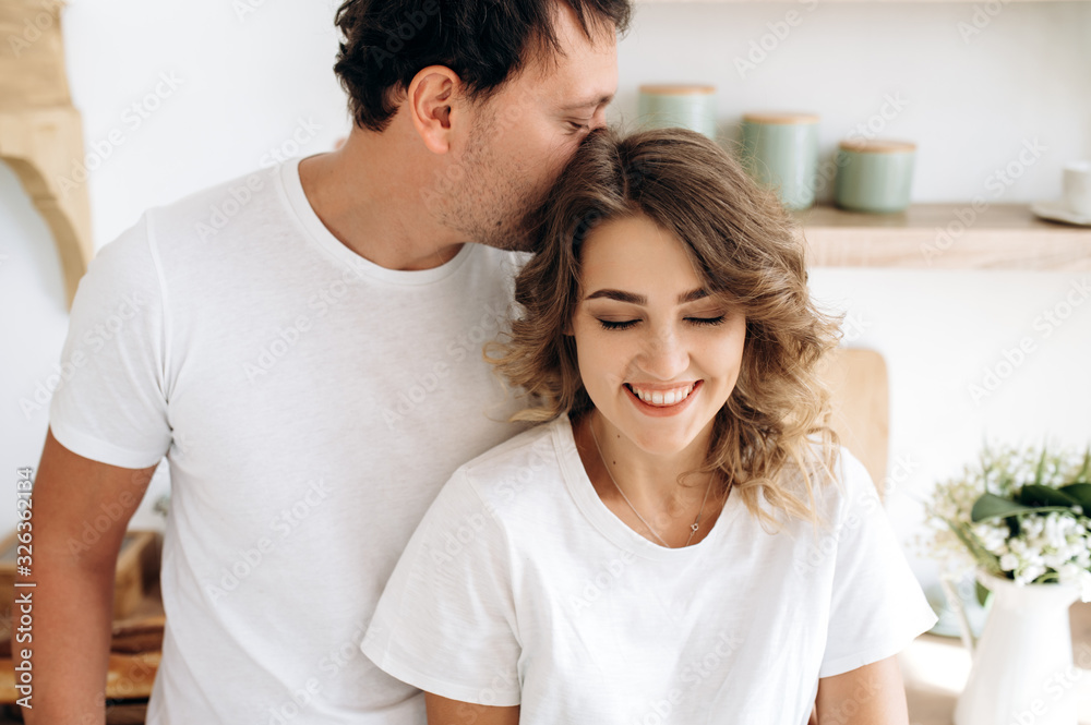 Close up portrait of an attractive couple in love in white t-shirts gently hugging in the kitchen Close up portrait of an attractive couple in love in white t-shirts gently hugging in the kitchen