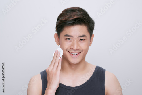 Handsome man cleaning face skin with batting cotton pads over white background and looking at camera photo