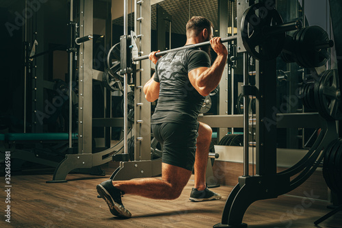 Fit man doing squats in a training machine