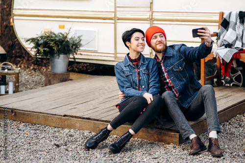Young hipster couple in love takes a selfie against the background of their trailer on which they are travel