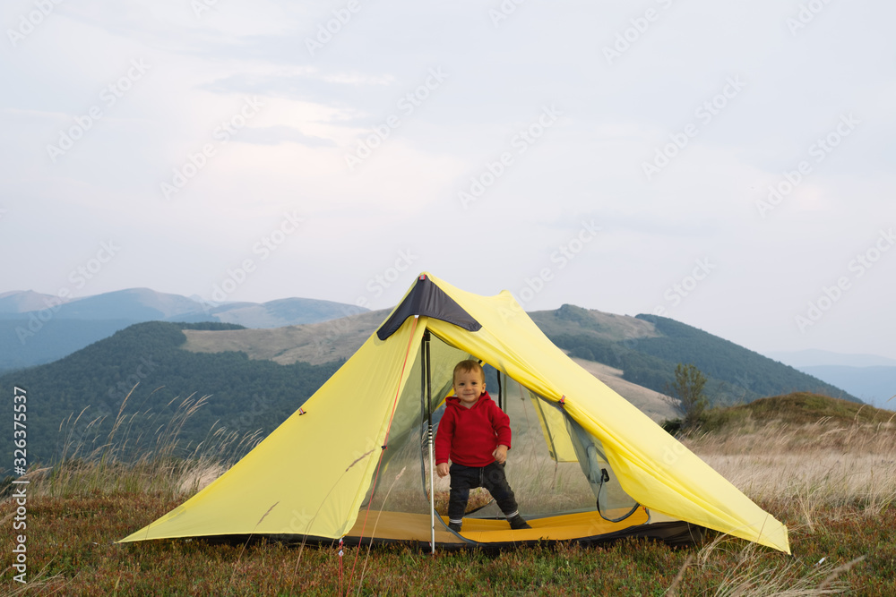 Small kid in yellow tent in spring mountains. Travel with child concept