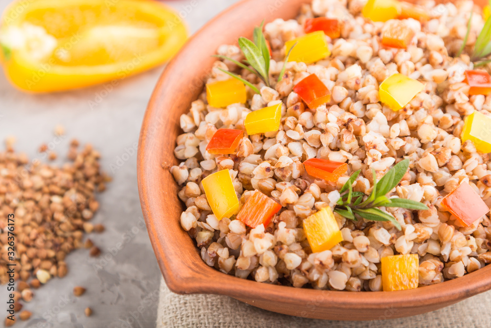 Buckwheat porridge with vegetables in clay bowl on a gray concrete background and linen textile. Side view, close up, selective focus. Buckwheat porridge with vegetables in clay bowl on a gray concrete background and linen textile. Side view, close up, selective focus.