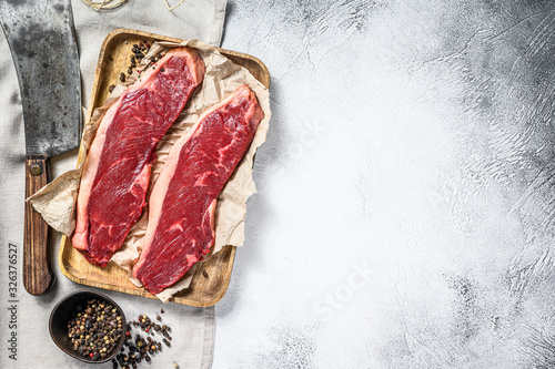 Raw sirloin steak on a wooden tray with a meat cleaver. Marble beef. Gray background. Top view. Copy space