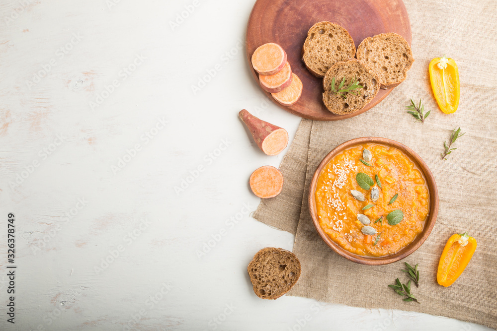 Sweet potato or batata cream soup with sesame seeds in a wooden bowl on a white wooden background. top view, copy space.