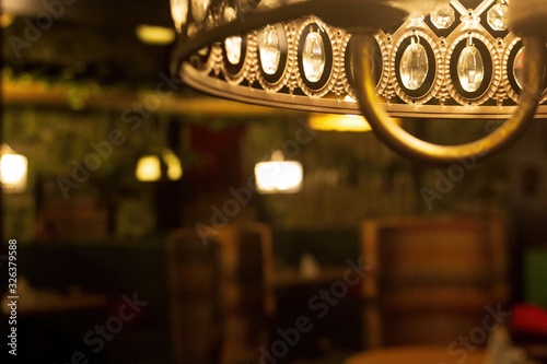 Concept of moody interior in the art deco style of the 1920s. The faint dim light of the golden chandelier barely illuminates the retro room. Selective focus with blurred copy spase