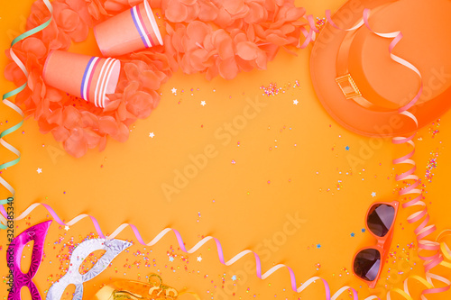 Decor for a traditional celebration of King's Day in the Netherlands. Orange hat, glasses, jewelry and confetti on a bright background. Picture in the form of a frame. Copy space. Flat lay photo