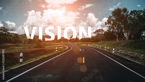 The word vision behind the tree of empty asphalt road at golden sunset and beautiful blue sky. Concept for vision. photo