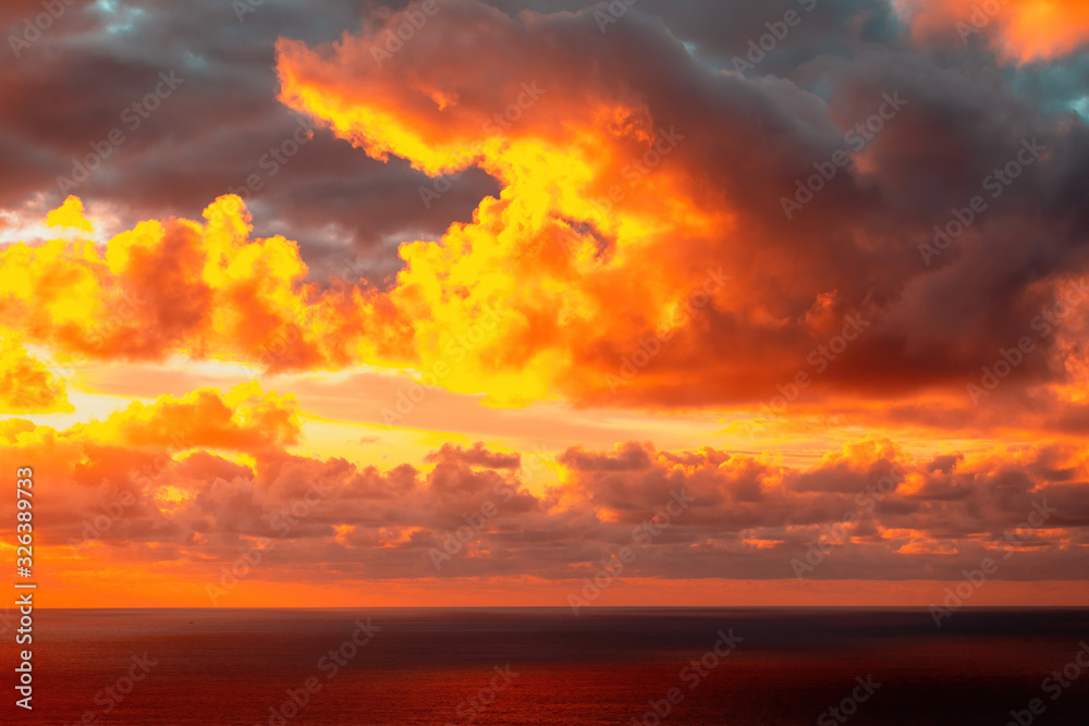 Aerial view of colorful clouds over horizon lit by sun setting into Pacific ocean at Piha beach