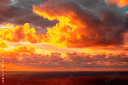 Aerial view of colorful clouds over horizon lit by sun setting into Pacific ocean at Piha beach © Emagnetic