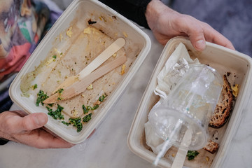 Man hands holding paper food containers, plastic cup, paper straw, wooden utensils to trash after meal, from above. Recycling, waste products, global enviromental issues concept. Take away, to-go food