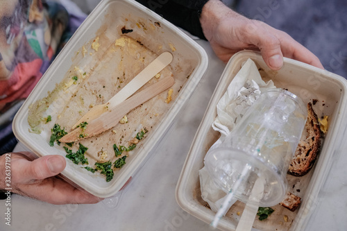 Man hands holding paper food containers, plastic cup, paper straw, wooden utensils to trash after meal, from above. Recycling, waste products, global enviromental issues concept. Take away, to-go food