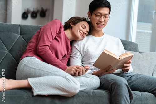 Photo of pleased multinational couple reading book and using smartphone