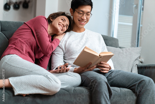 Photo of smiling multinational couple reading book and using smartphone