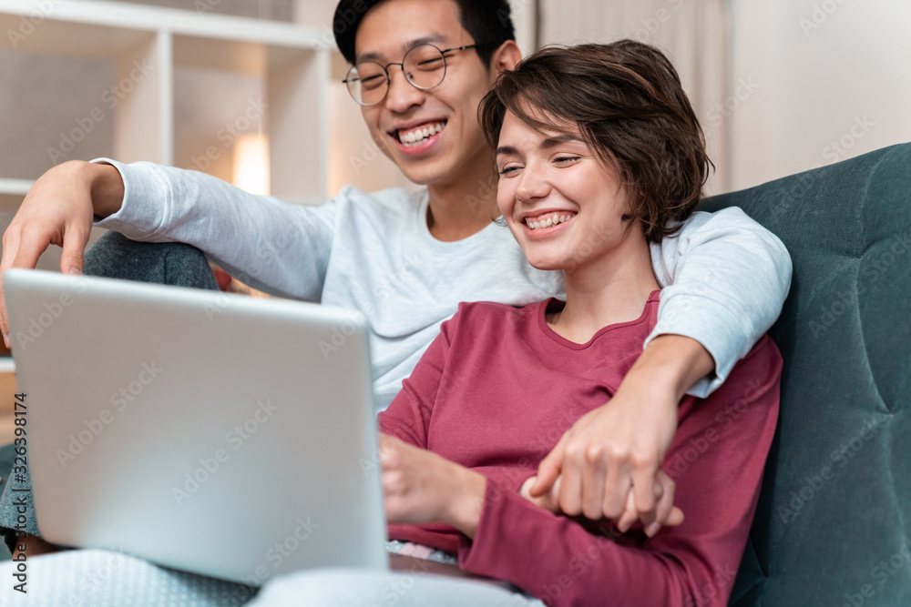 Photo of joyful multinational couple laughing and using laptop