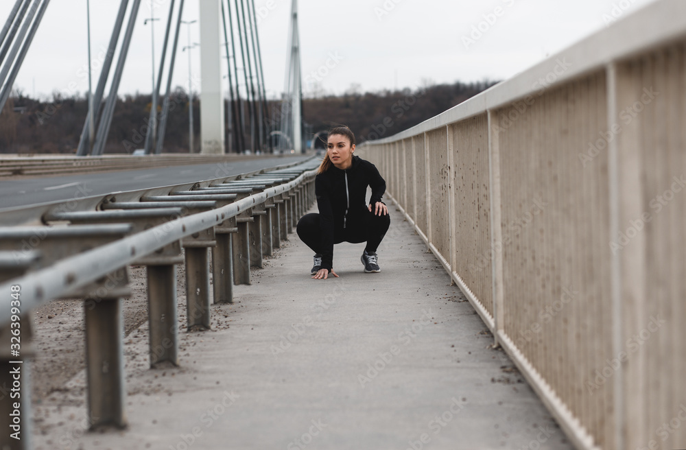 Young woman in black sports outfit resting after running on the bridge in the city.