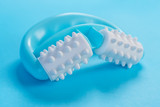 Turquoise plastic massager with white soft rollers and pimples on a blue creative background. Massage treatment for cellulite