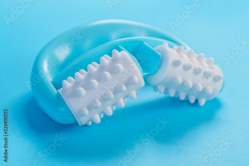 Turquoise plastic massager with white soft rollers and pimples on a blue creative background. Massage treatment for cellulite