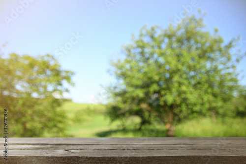 Image of grey wooden table in front of abstract blurred background of green leaves and trees
