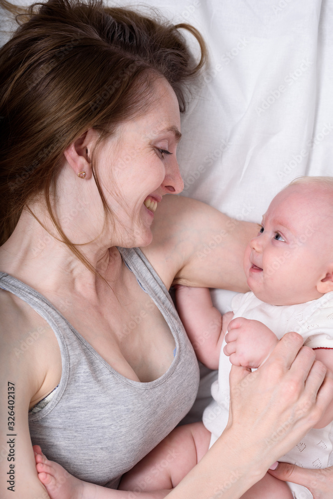 Happy loving young mother with her baby lying in bed. Portrait Top view Happy loving young mother with her baby lying in bed. Portrait Top view
