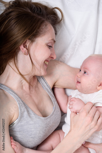 Happy loving young mother with her baby lying in bed. Portrait Top view