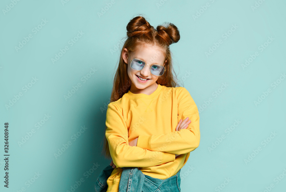 Nice smiling red-haired teen girl in blue glasses and yellow sweatshirt is standing with her arms crossed at chest Nice smiling red-haired teen girl in blue glasses and yellow sweatshirt is standing with her arms crossed at chest