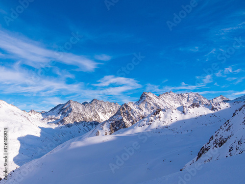 Alpine Winterlandschaft mit felsdurchsetzen Bergflanken und dunkelblauem Himmel mit Schleierwolken