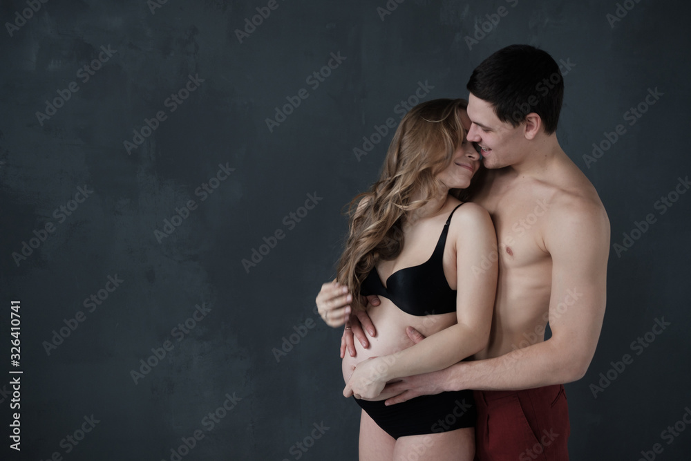 Naklejka premium Happy man embracing his pregnant girlfriend and looking at camera.